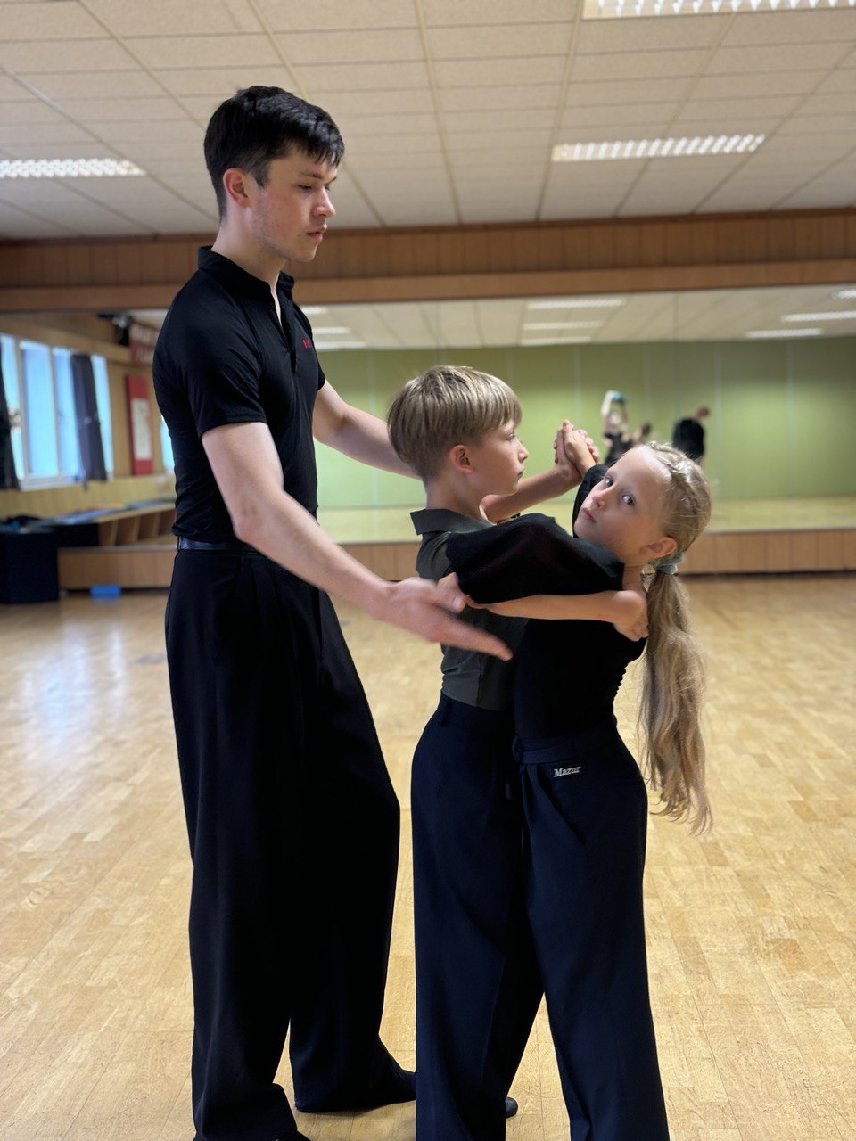 Coach teaching two young children a ballroom hold in the studio
