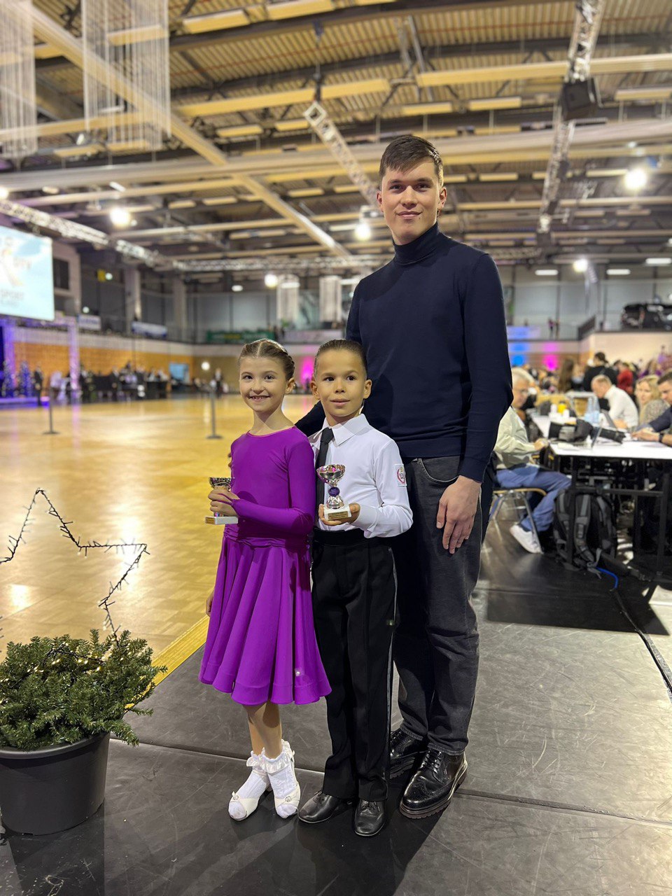 Coach with two young students holding their competition trophies